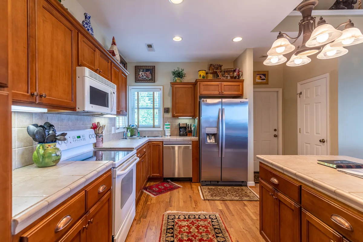 A spacious, well-stocked kitchen with wooden cabinetry, stainless steel appliances, a central island, and decorative rugs. The space is designed for both everyday cooking and festive gatherings, with ample room for meal preparation and socializing.