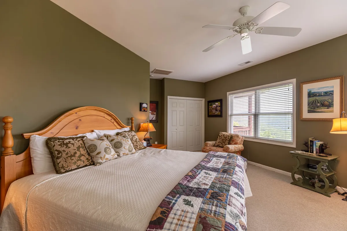 A tranquil bedroom with a comfortable bed adorned with decorative pillows, a reading chair near a window, and a softly lit nightstand. The window allows in natural light, creating a peaceful nook that invites relaxation, reading, or quiet contemplation.