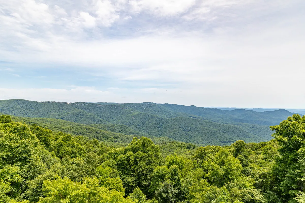 A wide, scenic shot captures an expansive mountain range framed by lush trees and distant hills, highlighting the natural beauty and adventure awaiting just beyond the home.