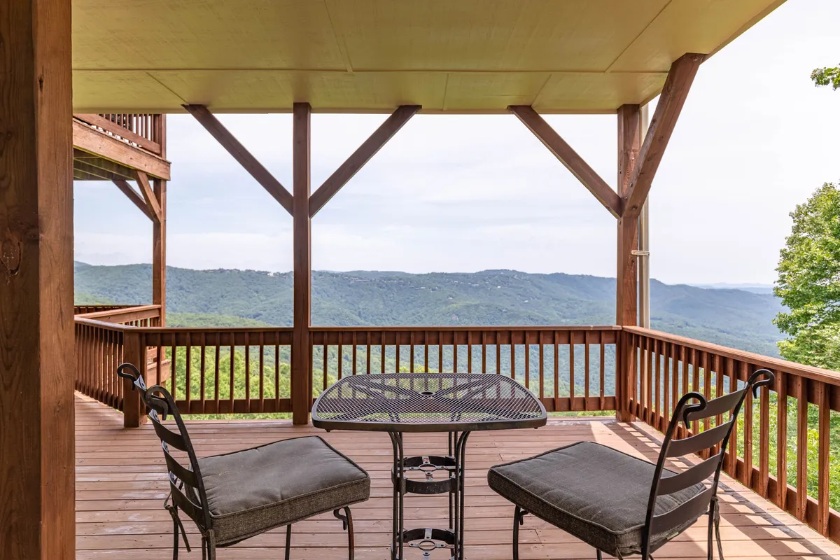 A wooden deck with seating overlooks scenic mountains, evoking tranquility and offering a peaceful spot for morning coffee or evening stargazing. The setting is ideal for relaxing, hosting intimate gatherings, or simply soaking in the view.