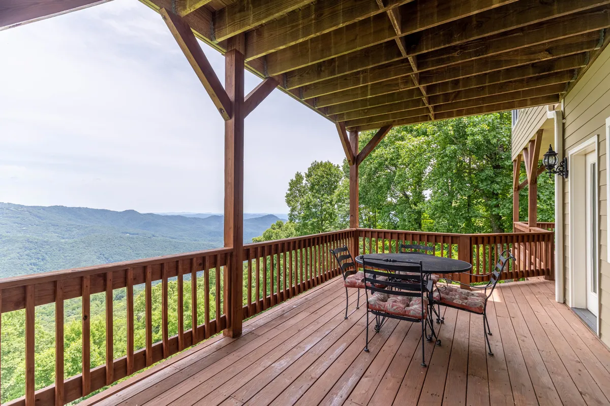 A spacious wooden deck overlooks rolling mountains, with comfortable outdoor seating arranged to maximize enjoyment of the view. The atmosphere is tranquil, making it ideal for socializing or quiet contemplation.