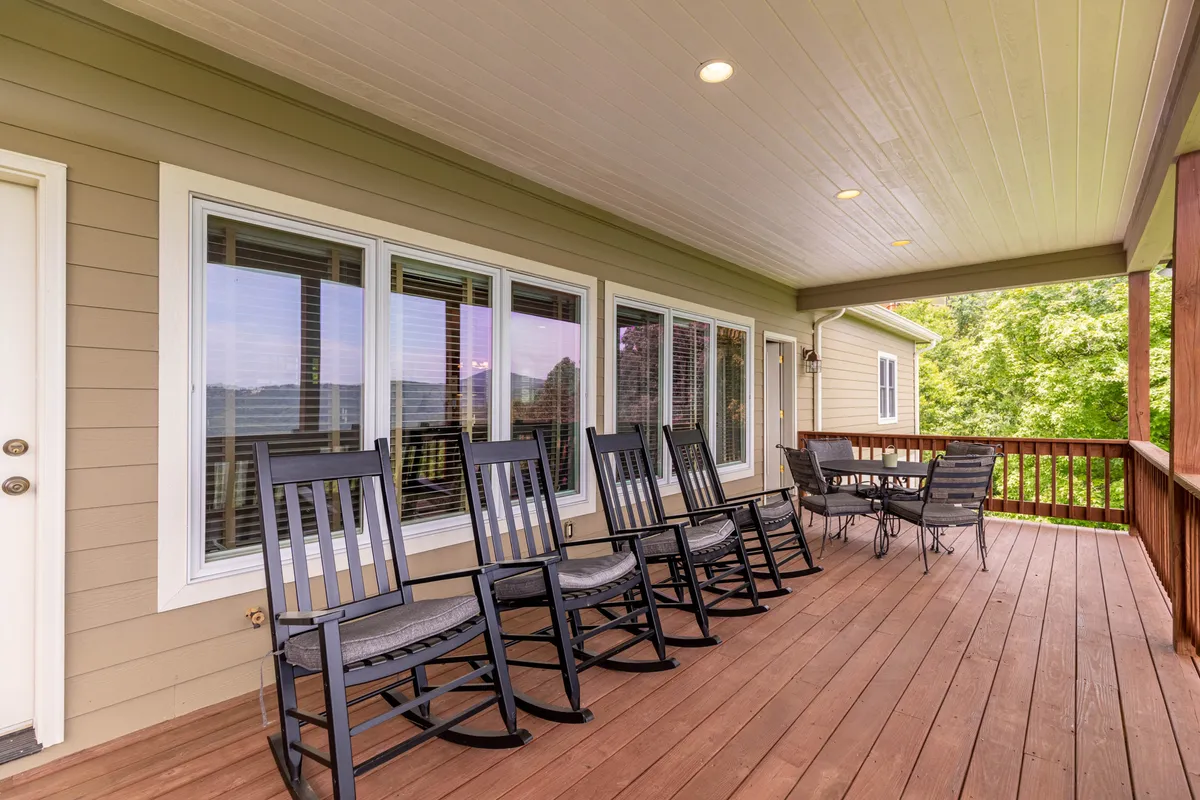 The image shows a spacious outdoor deck furnished with classic rocking chairs and a dining table, all set against a backdrop of expansive views and large windows reflecting the surrounding nature. The atmosphere is calm and serene, ideal for relaxation and connecting with the outdoors.
