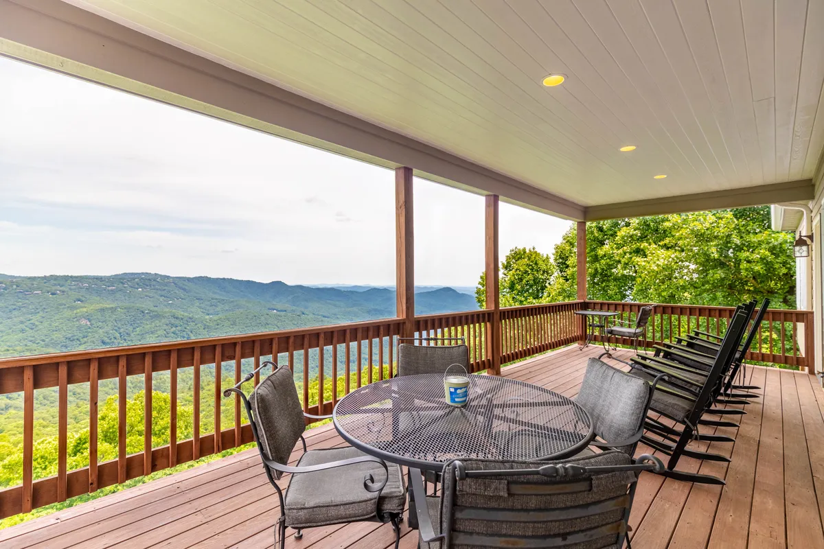 A serene covered deck with a dining table and rocking chairs overlooking sweeping mountain views. The space is ideal for outdoor dining, morning coffee, or simply relaxing while taking in the scenery of the John’s River Gorge.