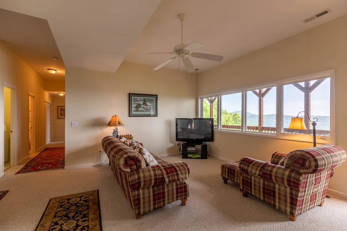 This cozy living room features plaid sofas positioned to face large windows that offer a view of the outdoors. Lamps provide warm light, and the arrangement encourages both relaxation and social interaction while maintaining a strong visual connection to the scenic surroundings through the windows.