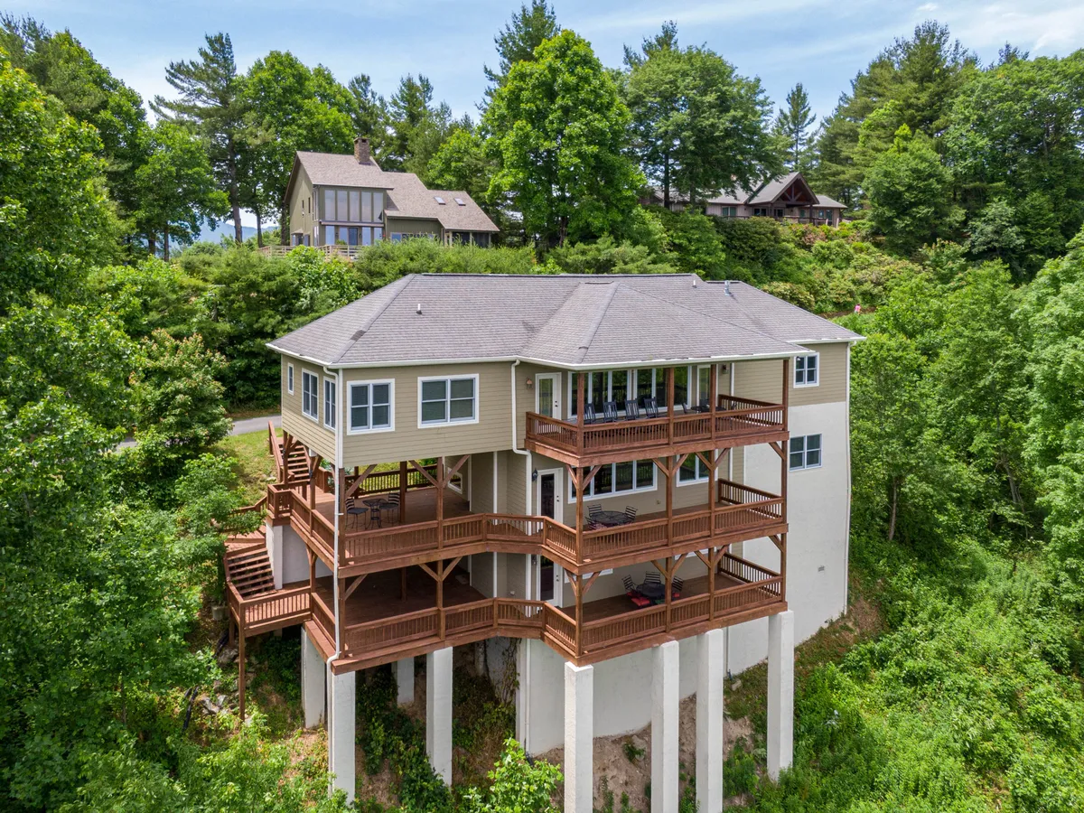 A multi-story deck surrounded by lush trees, showcasing the home's stylish exterior architecture. The deck is set up for outdoor dining and family gatherings, with ample seating and a welcoming, serene atmosphere. The image hints at the possibility of enjoying a sunset meal or relaxing outdoors together as a family.