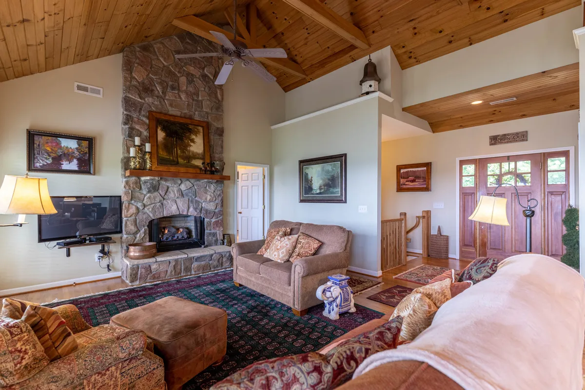 A cozy lounge area featuring a prominent stone fireplace, a comfortable sofa adorned with decorative cushions, and exposed wooden ceiling beams. The room exudes warmth and invites relaxation, with a layout perfect for gathering around the fire or enjoying quiet moments.
